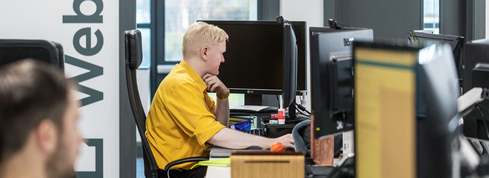 Man in a yellow shirt sat a desk using a computer for website development